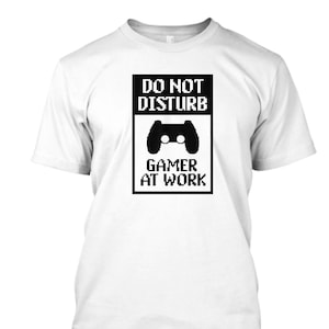 Könnte beinhalten: Weißes T-Shirt mit einer schwarz-weißen Grafik, auf der "Nicht stören Gamer bei der Arbeit" steht, mit einem pixelartigen Videospiel-Controller-Symbol.
