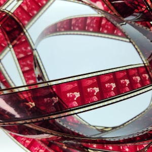 May include: Close-up of red and black film strips, showing the celluloid frames and sprocket holes. The film is wound in a circular pattern, creating a visual texture.