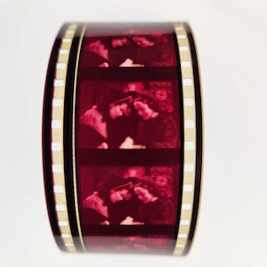 May include: A close-up of a film reel with multiple frames showing a couple in black and white. The film reel is red and has gold edges.