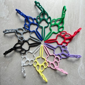 May include: A set of ten colorful paw print keychains. Each keychain is made of plastic and features a different color. The keychains are arranged in a circle, with the paw prints facing outwards.