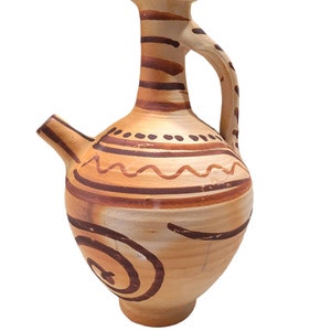 May include: A tan ceramic pitcher with a brown handle and spout. The pitcher is decorated with brown horizontal stripes, wavy lines, and a spiral design. The top of the pitcher is dark brown.