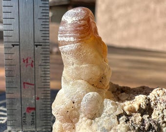Może przedstawiać: Geoda agatowa w kolorze brązowym i białym z paskowanym wzorem. Geoda ma około 5 cm wysokości i stoi na czarnym tle.