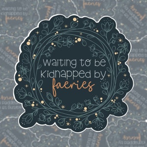 May include: A dark blue sticker with a floral wreath design. The text "Waiting to be Kidnapped by faeries" is written in a light brown font.