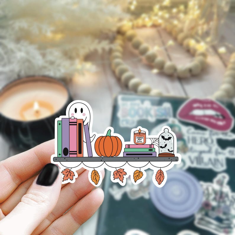 May include: A sticker featuring a bookshelf with a ghost, pumpkin, books, a candle that says "Pumpkin Spice Latte", and a glass dome with bats. The shelf is decorated with fall leaves.