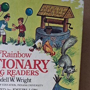 Może przedstawiać: Okładka książki The Rainbow Dictionary for Young Readers przedstawia kolorowe ilustracje zwierząt, zamku, studni i tipi. Tytuł książki jest pogrubiony, czarnymi literami z wzorem tęczy. Okładka książki jest żółta z zielonymi obramowaniami.