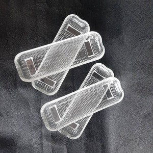 May include: Four clear plastic rectangular trays with a textured surface. The trays are stacked on top of each other.