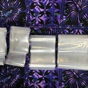 May include: A set of clear plastic bags of various sizes, ideal for packaging small items. The bags are flat and lie on a purple and black patterned surface.