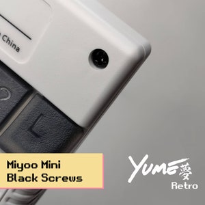 以下が含まれることがあります： 「L」と「L2」とラベル付けされた黒いボタンが付いた白いゲームコンソールのクローズアップ。コンソールは右上の角に黒いネジがあります。左上の角に「Made in China」というテキストが表示されています。コンソールの下に黄色のボックスに「Miyoo Mini Black Screws」というテキストが表示されています。グレーの背景に白い「Yume Retro」というテキストが表示されています。