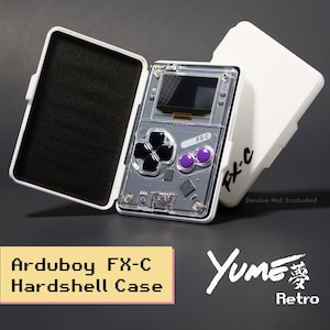 May include: A white hardshell case for an Arduboy FX-C handheld gaming device. The case is open, revealing a black foam interior, and is shown next to a closed white case labeled FX-C. The device itself has a clear casing, black D-pad, and purple buttons.