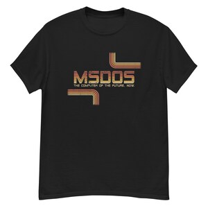 Puede incluir: Camiseta negra con el texto "MSDOS THE COMPUTER OF THE FUTURE. NOW." en una fuente retro con líneas naranjas y amarillas. La camiseta es de cuello redondo.