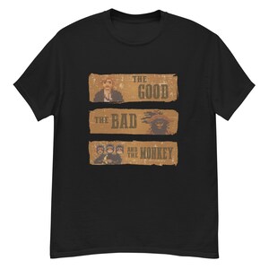 May include: Black t-shirt featuring a pixelated design with the text "THE GOOD", "THE BAD", and "AND THE MONKEY". The design includes pixelated images of a person, a monkey, and other figures. A unique graphic tee.