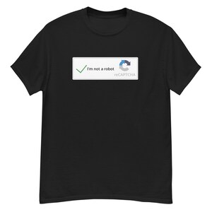Peut inclure: T-shirt noir avec un rectangle blanc portant l'inscription "I'm not a robot" et une coche verte. Le logo reCAPTCHA est également visible. Le t-shirt est de style col rond.