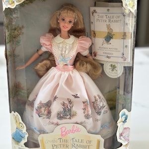 May include: Collector Edition Barbie doll in a clear display box. The doll has blonde hair and wears a pink dress with illustrations from "The Tale of Peter Rabbit." The box includes a miniature book and the text "First in a Collection of Keepsake Treasures."