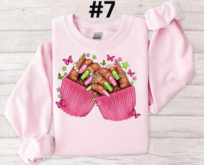 May include: Pink sweatshirt with a graphic of two hands with green and pink nail polish, rings, and butterflies. The text #7 is in the top center of the image.