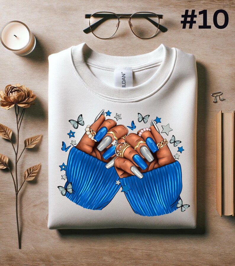 May include: White sweatshirt with a blue and white illustration of two hands with long, blue and silver painted nails. The hands are wearing rings and are surrounded by stars and butterflies.