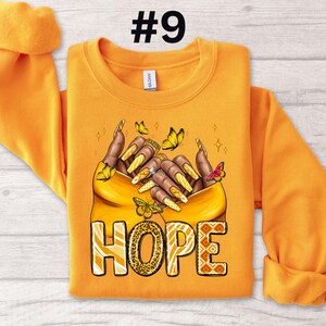 May include: Orange sweatshirt with a graphic of two hands holding each other with butterflies and the word "HOPE" in a leopard print design.