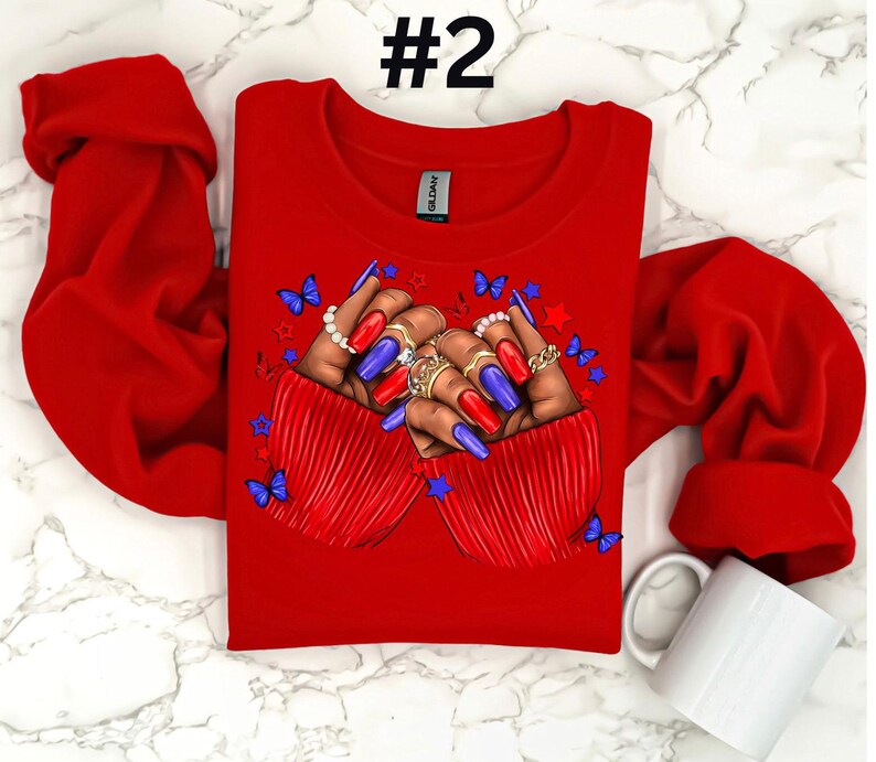 May include: Red long-sleeve shirt with a graphic of two hands with blue and red nail polish, rings, and butterflies. The hands are clasped together in a heart shape. The shirt has the number "#2" printed on the top.
