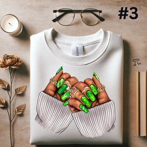 May include: White sweatshirt with a graphic of two hands with long green manicured nails and rings. The hands are in a heart shape.