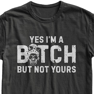 May include: Dark gray t-shirt with the text "YES I'M A BITCH BUT NOT YOURS" in distressed white lettering. The word "BITCH" features a skull wearing sunglasses and a headband. A casual, edgy graphic tee.