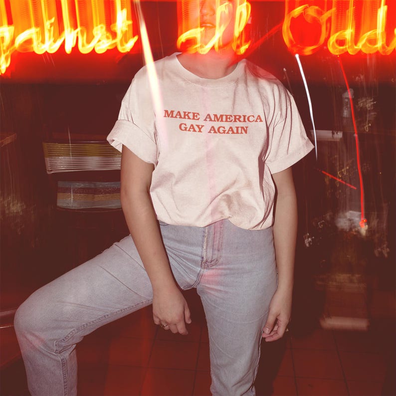 Peut inclure: Un t-shirt blanc avec le texte "Make America Gay Again" imprim&eacute; en rouge.