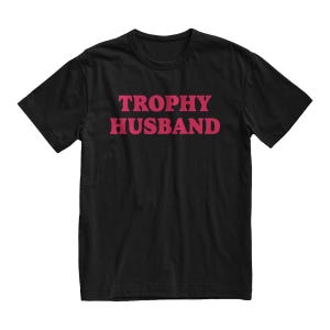 May include: Black t-shirt with the text "TROPHY HUSBAND" in pink letters.