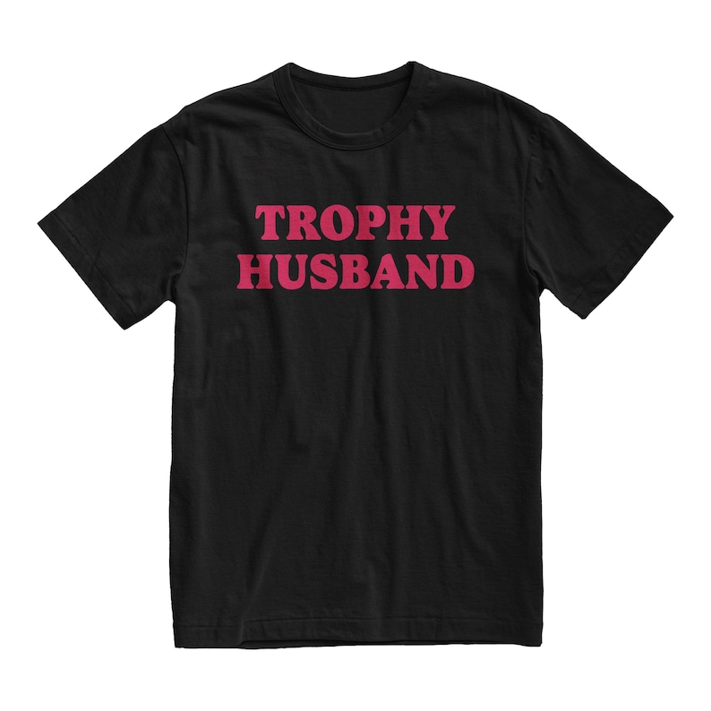 May include: Black t-shirt with the text "TROPHY HUSBAND" in pink letters.