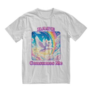 May include: A white t-shirt with a graphic of a white cat with wings flying through a rainbow. The text "RAGE CONSUMES ME" is printed in pink below the graphic.