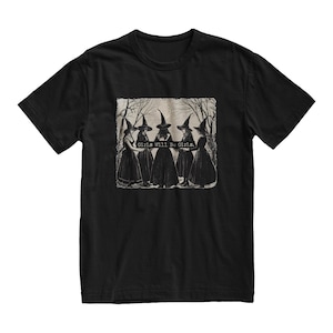 K&ouml;nnte beinhalten: Schwarzes T-Shirt mit einem grafischen Druck von f&uuml;nf Hexen, die schwarze spitze H&uuml;te und Kleider tragen. Der Text "Girls Will Be Girls." ist auf dem Grafikdruck.