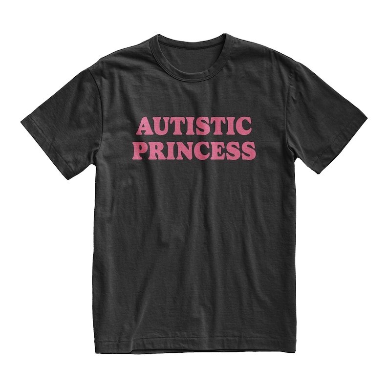 Puede incluir: Camiseta negra con el texto rosa "AUTISTIC PRINCESS" en el pecho. El texto est&aacute; en negrita, sin serifa. La camiseta tiene mangas cortas y cuello redondo.