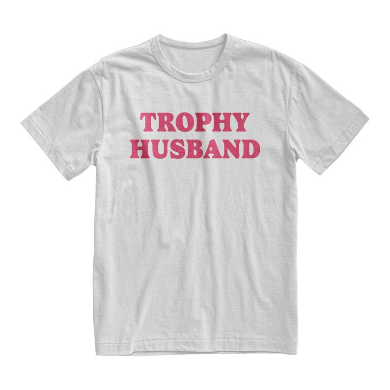 May include: White t-shirt with the text "TROPHY HUSBAND" printed in pink.