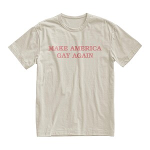 Peut inclure: Un t-shirt beige clair avec le texte "MAKE AMERICA GAY AGAIN" imprim&eacute; en rose.
