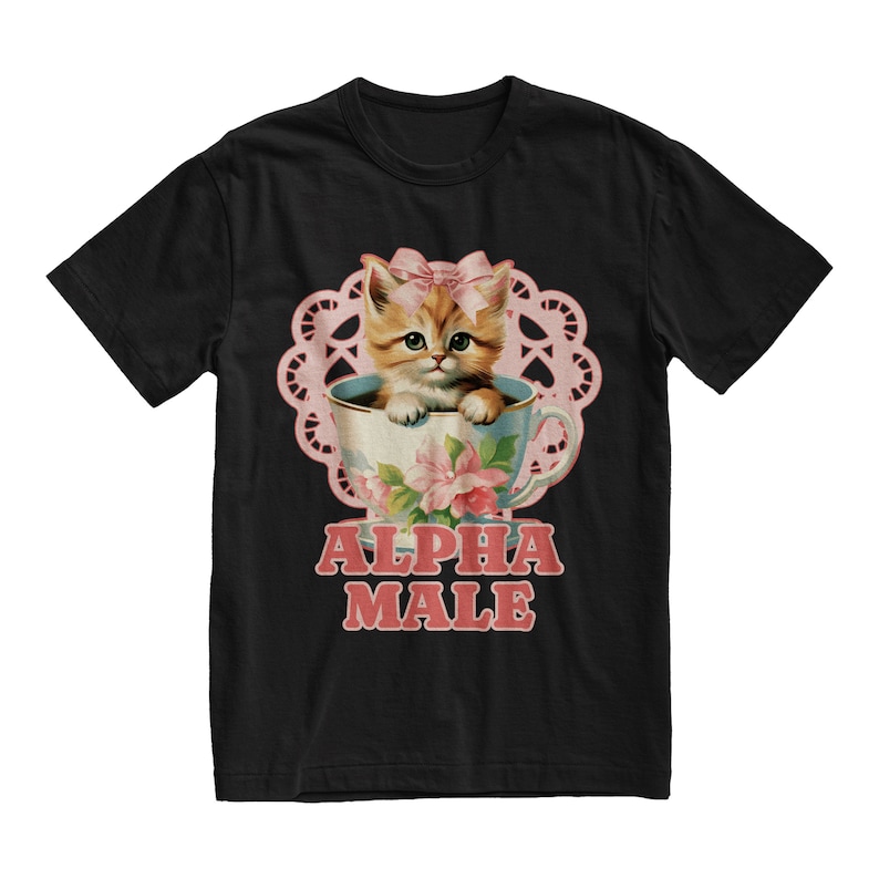 Pu&ograve; includere: Maglietta nera con un'illustrazione rosa e bianca di un gattino in una tazza da t&egrave;. Il testo "ALPHA MALE" &egrave; stampato in lettere rosa sotto l'immagine.