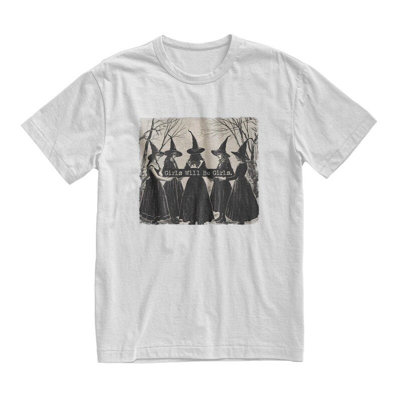 K&ouml;nnte beinhalten: Wei&szlig;es T-Shirt mit einer Schwarzwei&szlig;illustration von f&uuml;nf Hexen, die schwarze spitze H&uuml;te und Kleider tragen. Der Text "Girls Will Be Girls." ist auf das T-Shirt gedruckt.
