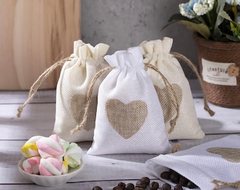 May include: A collection of small, drawstring burlap bags, some filled with coffee beans and others with marshmallows. Each bag features a printed heart design. The bags are in shades of white and beige, with natural twine drawstrings.