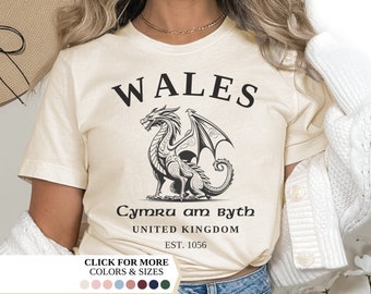 Puede incluir: Una camiseta de color crema con un gráfico de dragón negro y el texto "WALES Cymru am Byth UNITED KINGDOM EST. 1056".