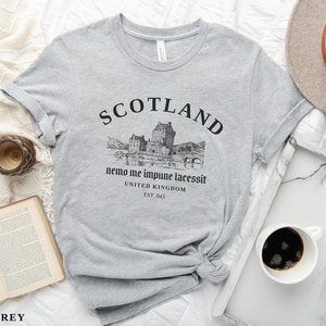 May include: Athletic grey t-shirt with a graphic of a Scottish castle and the word "SCOTLAND" in black. The shirt also features the text "nemo me impune lacessit" and "UNITED KINGDOM EST. 843".