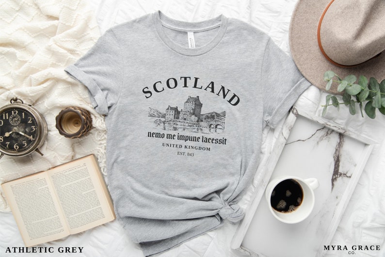 May include: Athletic grey t-shirt with a graphic of a Scottish castle and the word "SCOTLAND" in black. The shirt also features the text "nemo me impune lacessit" and "UNITED KINGDOM EST. 843".
