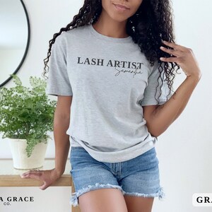 Pu&ograve; includere: Una maglietta grigia con la scritta "LASH ARTIST Samantha" in nero. La maglietta &egrave; a maniche corte e realizzata in un materiale morbido. L'angolo in basso a destra dell'immagine ha la parola "GRAY" in un riquadro bianco.