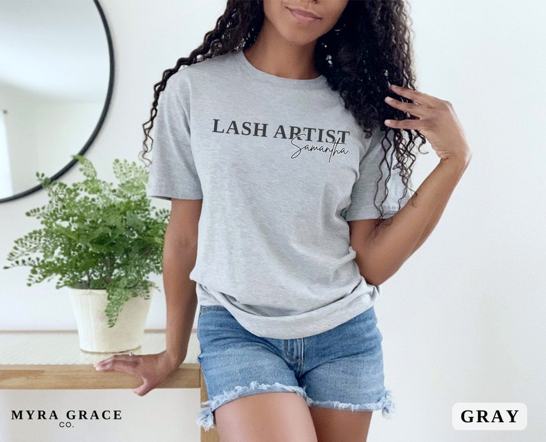 Pu&ograve; includere: Una maglietta grigia con la scritta "LASH ARTIST Samantha" in nero. La maglietta &egrave; a maniche corte e realizzata in un materiale morbido. L'angolo in basso a destra dell'immagine ha la parola "GRAY" in un riquadro bianco.