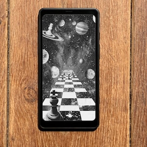 Pode incluir: Um smartphone preto exibe uma imagem em preto e branco de um tabuleiro de xadrez que se estende para o espaço, rodeado por planetas e estrelas. As peças de xadrez estão posicionadas no tabuleiro. O telefone está sobre uma superfície de madeira.