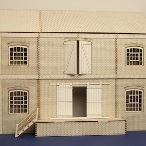 Pode incluir: Um edifício de tijolo bege de dois andares com uma grande porta de madeira e janelas. O edifício tem um pequeno conjunto de escadas que levam à porta.