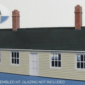 May include: Unpainted and unassembled model kit of a small, white, two-story building with a green roof and two brick chimneys. The kit includes windows, doors, and other details. "UNPAINTED AND UNASSEMBLED KIT, GLAZING NOT INCLUDED" is printed on the bottom of the image.