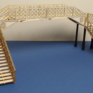 May include: A wooden model of a footbridge with two sets of stairs leading up to the bridge. The bridge has a lattice design and is supported by four black pillars.