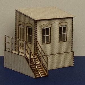 Puede incluir: Un pequeño modelo de madera beige de un edificio con techo plano, dos ventanas y una puerta. El edificio tiene una fachada de ladrillo y una escalera que conduce a la puerta. El modelo está sobre una superficie azul.