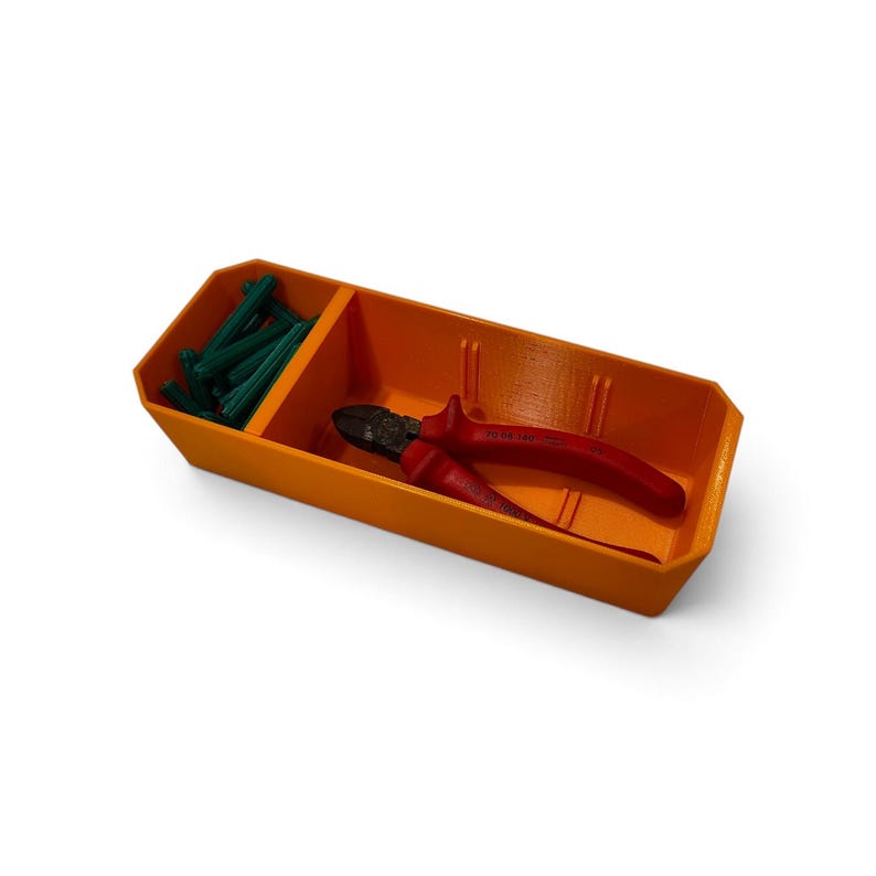 May include: An orange rectangular plastic storage tray with two compartments. The smaller section contains several green plastic wall anchors, while the larger section holds a pair of red and black wire cutting pliers with metal jaws.
