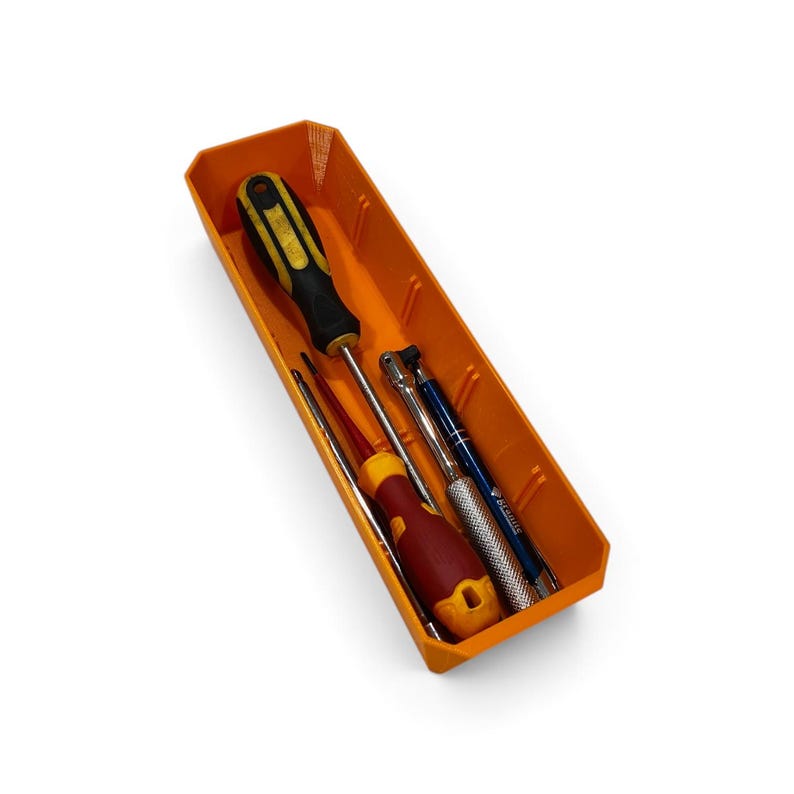 Op de afbeelding: Een oranje rechthoekige plastic opbergbak met vier gereedschappen: een gele en zwarte schroevendraaier, een rode en gele schroevendraaier, een zilveren metalen ratelhandvat met een getextureerde grip en een blauw en zilverkleurig penvormig gereedschap.