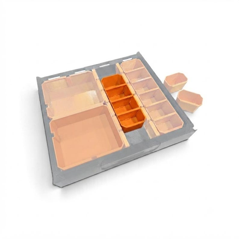 May include: A grey drawer organiser insert featuring a large square compartment, a central row of four vibrant orange rectangular bins, and a side row of five smaller light peach rectangular bins, with two additional loose bins placed nearby.