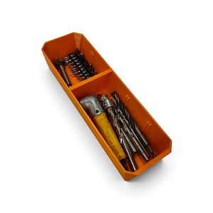 Op de afbeelding: Een oranje rechthoekige opbergbak met twee compartimenten. Het kleinere gedeelte bevat een rij metalen schroefbits. Het grotere gedeelte bevat een geel haaks boorhulpstuk en diverse metalen boortjes van verschillende afmetingen.