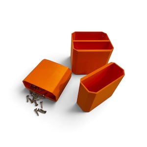 May include: Three bright orange, geometric, open-top storage containers with faceted sides. One container is lying on its side with several small metal screws spilling out from the opening, while the other two stand upright.