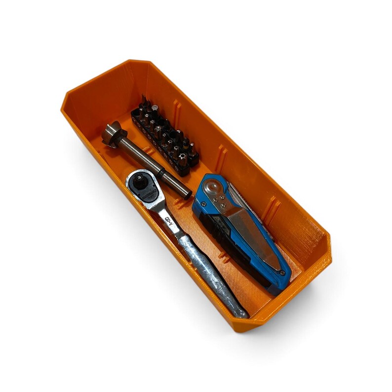 May include: A bright orange rectangular storage tray containing a silver metal ratchet, a black and blue folding utility knife, and a black plastic holder filled with various small metal screwdriver bits arranged in a single row.